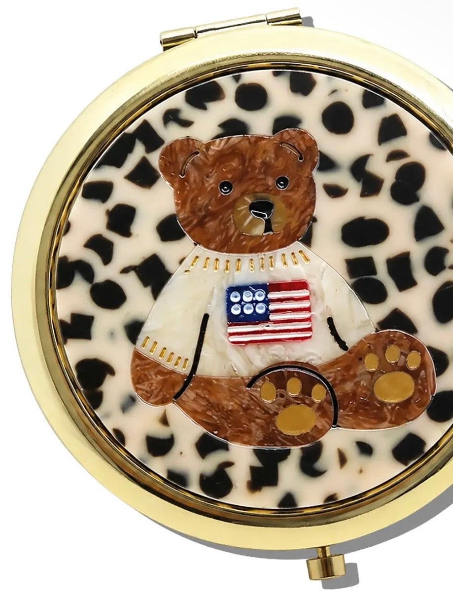 Round gold compact mirror featuring a leopard print background with a brown teddy bear wearing an American flag sweater.