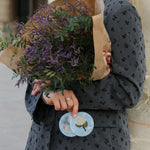 Light blue marbled compact mirror with floral brooch detail, held by woman in grey floral blazer.