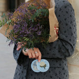 Light blue marbled compact mirror with floral brooch detail, held by woman in grey floral blazer.