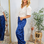 Woman wearing white cropped button-up shirt with blue wide-leg denim pants featuring shell print details, styled with layered