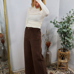 Chocolate brown wide-leg corduroy pants styled with a white turtleneck, shown on a model with tan ankle boots.