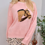 Woman wearing a soft pink knit sweater with an embroidered horse head graphic on the chest
