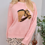 Woman wearing a soft pink knit sweater with an embroidered horse head graphic on the chest