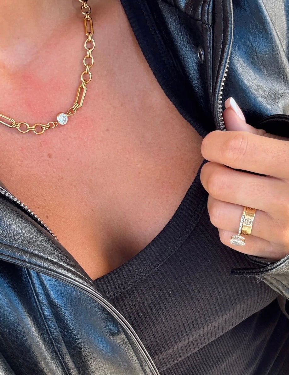Gold mixed chain-link necklace with single bezel-set diamond pendant, worn over black ribbed top with leather jacket.