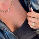 Gold mixed chain-link necklace with single bezel-set diamond pendant, worn over black ribbed top with leather jacket.