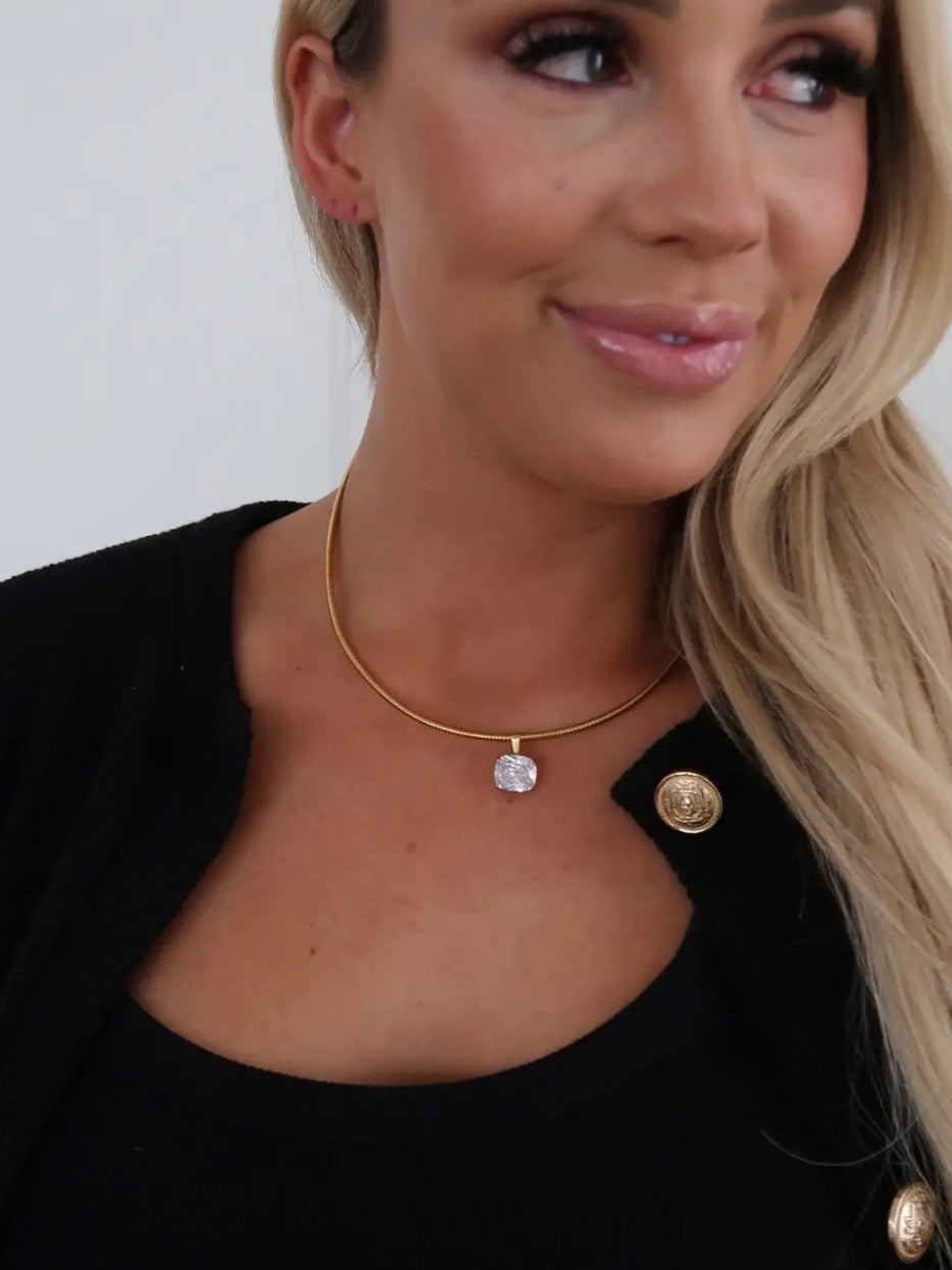Gold snake chain necklace with cushion-cut crystal pendant, styled on model wearing black blazer.