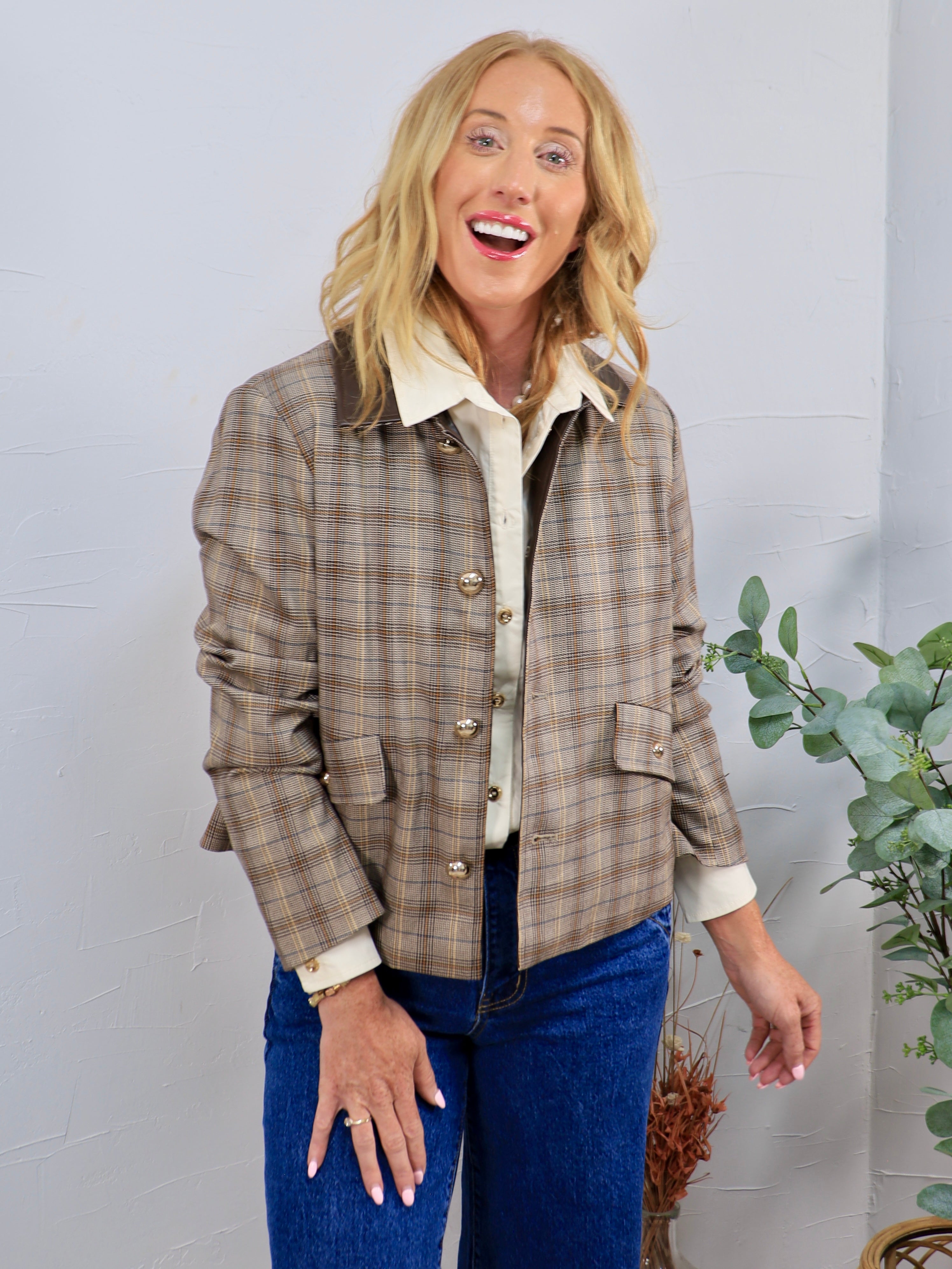 Tan plaid button-front jacket with gold buttons, styled over cream shirt and blue jeans.