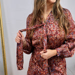 Burgundy floral satin mini dress with long sleeves, tie neck detail, and ruffle hem, shown on model.