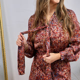 Burgundy floral satin mini dress with long sleeves, tie neck detail, and ruffle hem, shown on model.