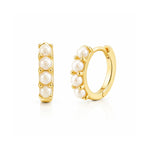 Gold tone huggie hoop earrings with four white pearls on white background