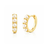 Gold tone huggie hoop earrings with four white pearls on white background