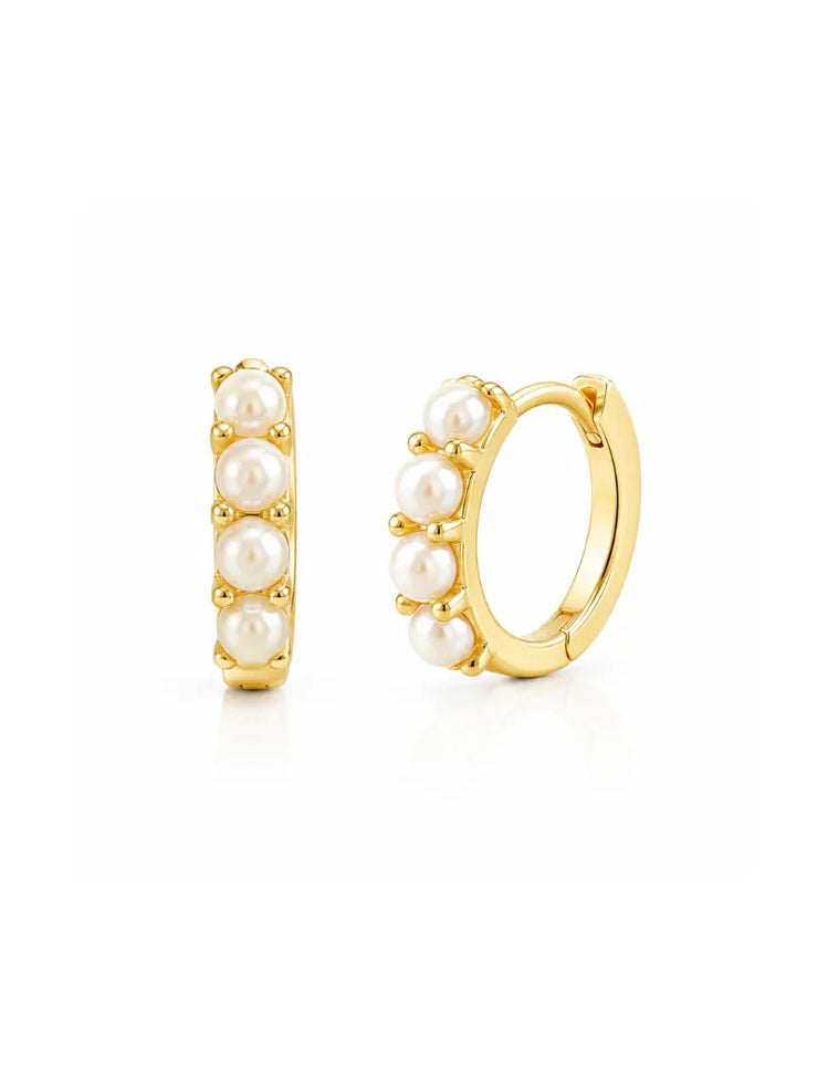 Gold tone huggie hoop earrings with four white pearls on white background