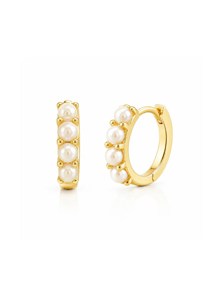 Gold tone huggie hoop earrings with four white pearls on white background