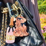 Two acrylic keychains featuring a rosé bottle and Cocker Spaniel charm on a black quilted handbag