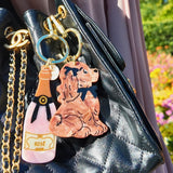 Two acrylic keychains featuring a rosé bottle and Cocker Spaniel charm on a black quilted handbag