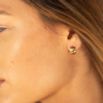 Woman wearing small gold huggie hoop earrings, shown in profile with blonde hair and warm natural lighting.