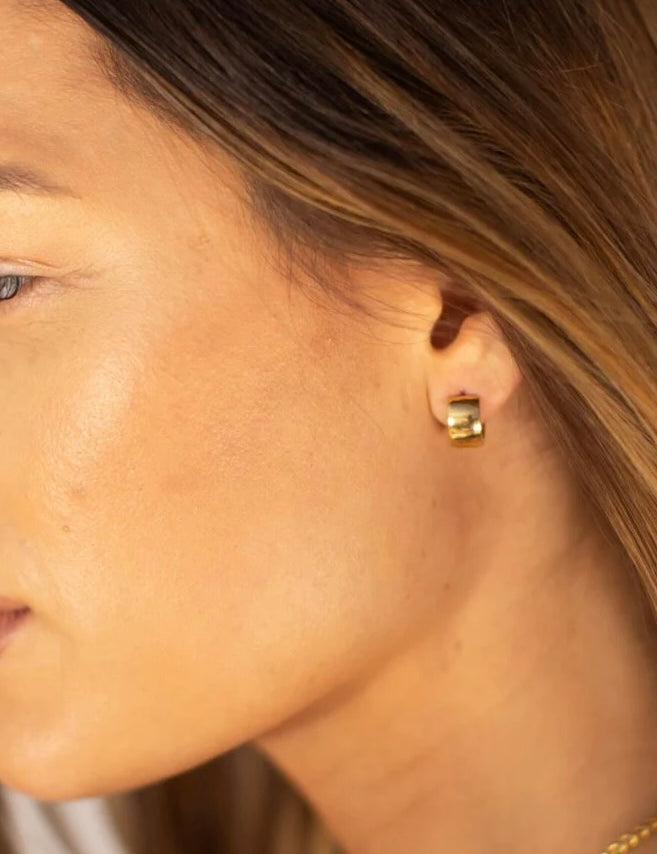 Woman wearing small gold huggie hoop earrings, shown in profile with blonde hair and warm natural lighting.