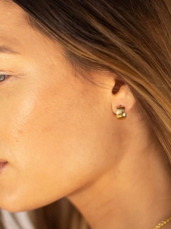 Woman wearing small gold huggie hoop earrings, shown in profile with blonde hair and warm natural lighting.
