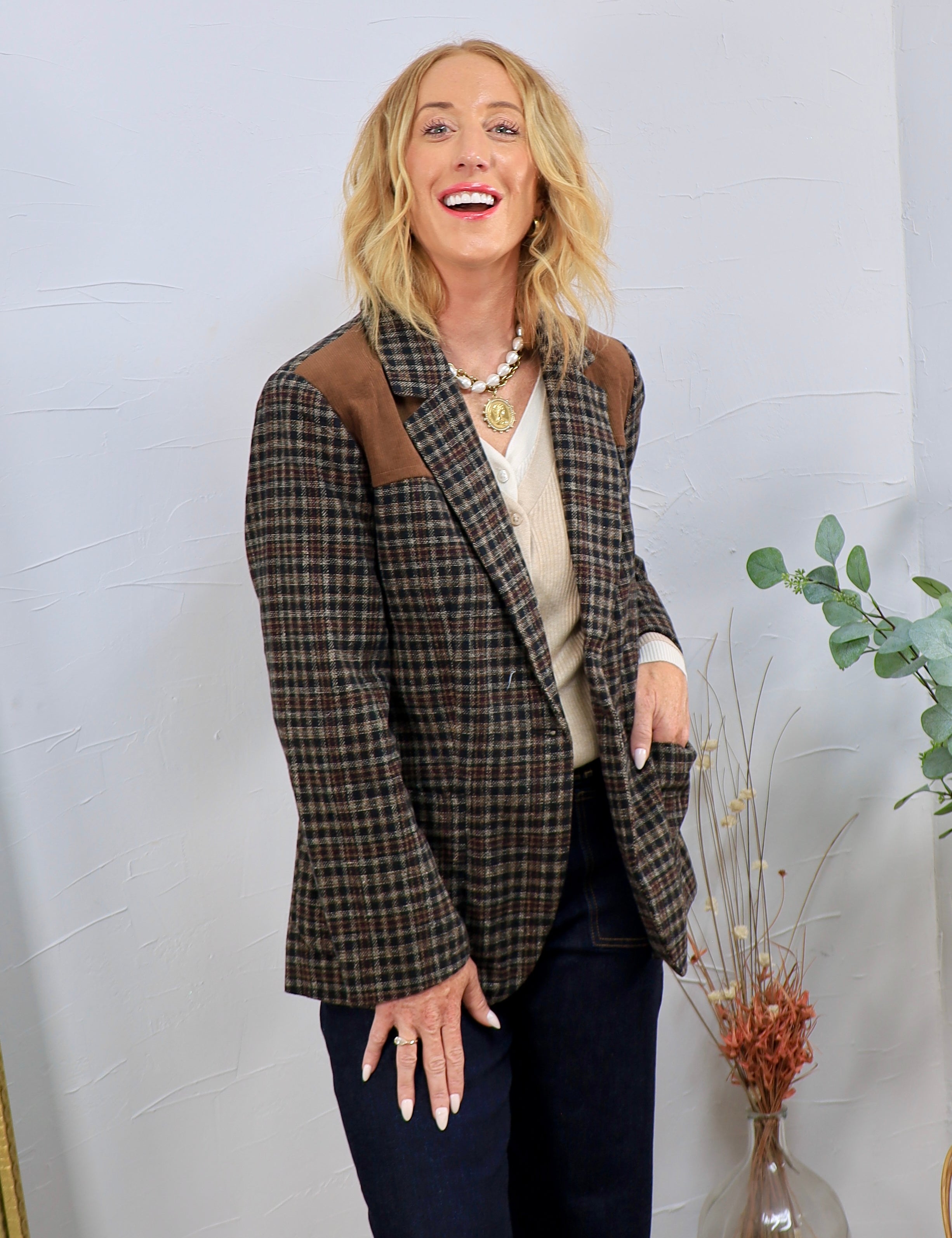 Brown plaid wool blazer with suede shoulder patches, styled over cream sweater and dark jeans.