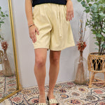 Woman wearing soft butter yellow pleated shorts with navy crochet top and studded slide sandals