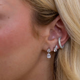 Clear crystal pear-shaped drop earrings worn on blonde woman's ear, silver-tone setting