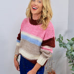 Woman wearing a chunky multicolor striped crewneck knit sweater with blue jeans, smiling