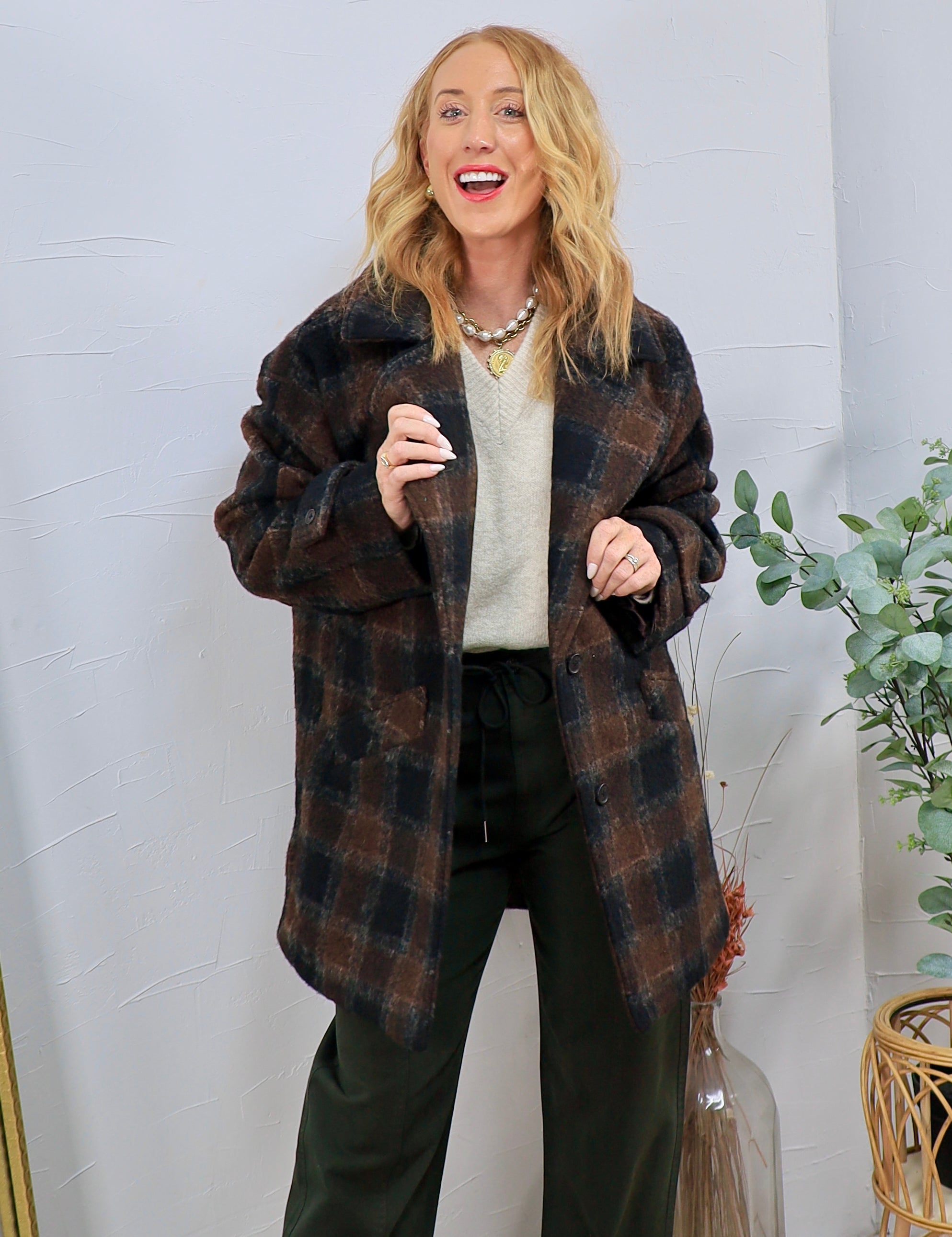 Oversized brown and black plaid shacket styled open over cream sweater and dark trousers with gold jewelry.