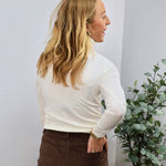 White long sleeve fitted turtleneck top styled with brown corduroy pants, shown from the back.