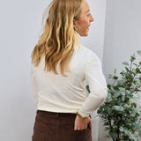 White long sleeve fitted turtleneck top styled with brown corduroy pants, shown from the back.