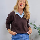 Woman wearing a chocolate brown v-neck sweater layered over a light blue collared shirt with jeans