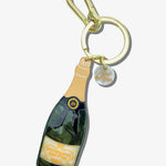 Solar Eclipse champagne bottle keychain with gold carabiner clip, green resin bottle charm, and branded tag.