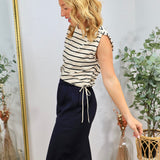 Woman wearing white and black striped sleeveless top with tie waist detail, paired with navy wide-leg pants, styled with blon