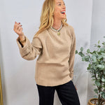 Camel beige crewneck sweater with ribbed hem and cuffs, styled with black wide-leg trousers and pearl necklace.