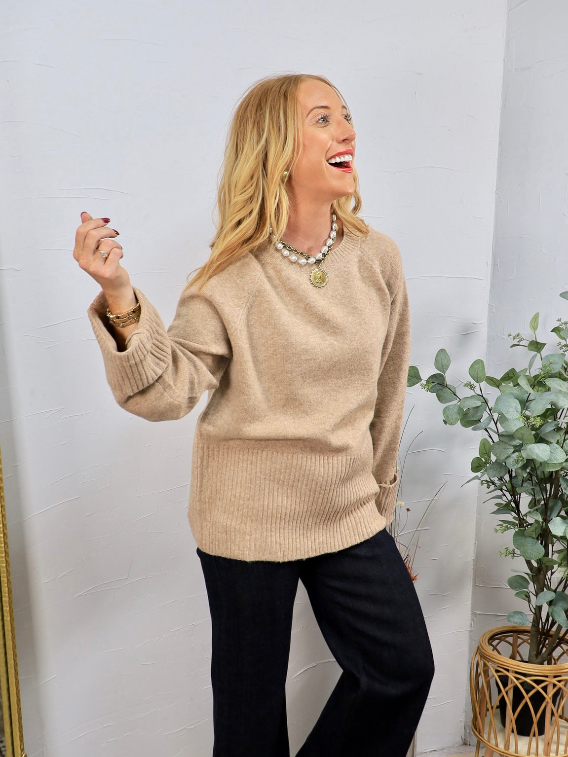 Camel beige crewneck sweater with ribbed hem and cuffs, styled with black wide-leg trousers and pearl necklace.