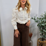Woman wearing cream puff-sleeve button-front blouse tucked into wide-leg brown corduroy trousers
