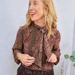 Woman wearing dark olive floral paisley long sleeve blouse with neck tie detail and dark leather pants