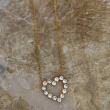 Gold chain necklace with open heart pendant formed by round sparkling clear crystal stones on marble surface.