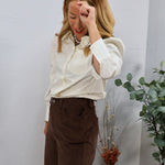 Ivory cream blouse with puff shoulders and wide cuffs, tucked into brown corduroy wide-leg pants.