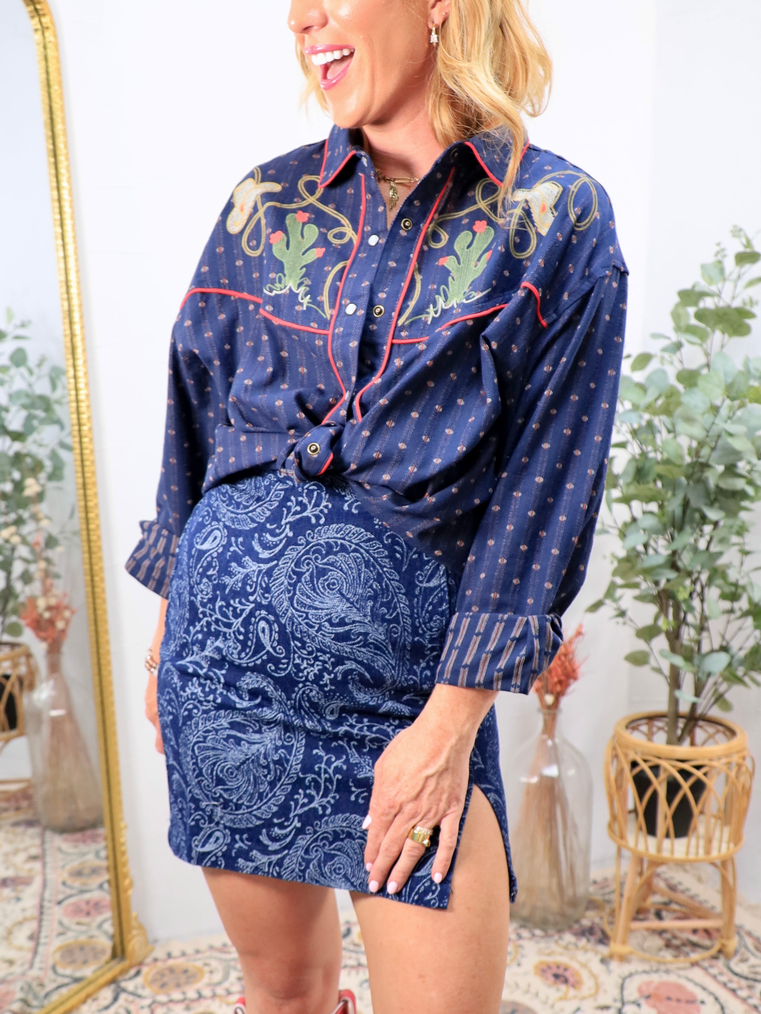 Woman wearing navy western snap button shirt with cactus embroidery and red piping trim