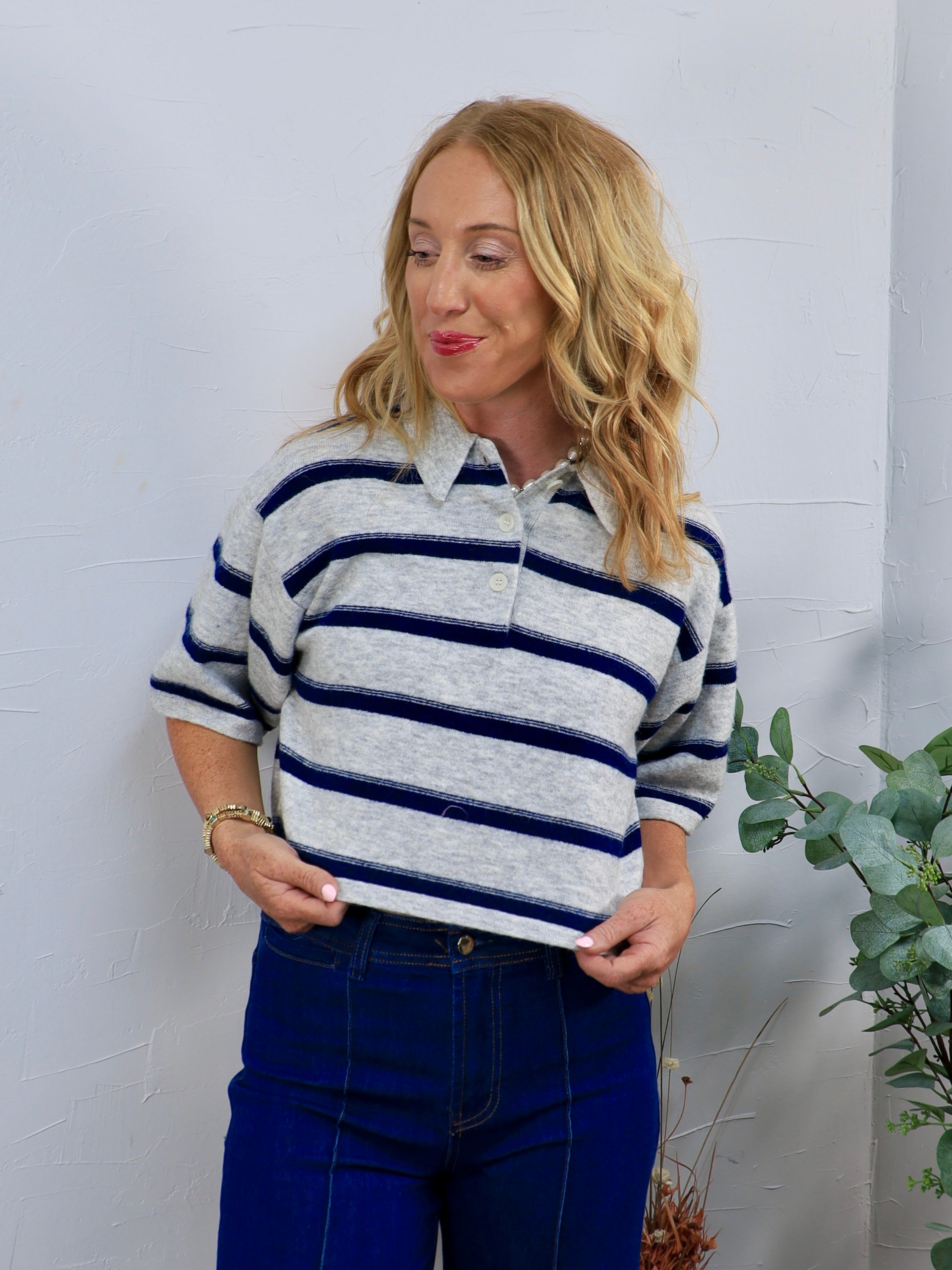 Gray and navy striped short-sleeve rugby polo sweater, styled with dark blue high-waisted jeans.