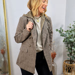 Woman wearing a brown plaid double-breasted blazer with removable hoodie layer over dark jeans