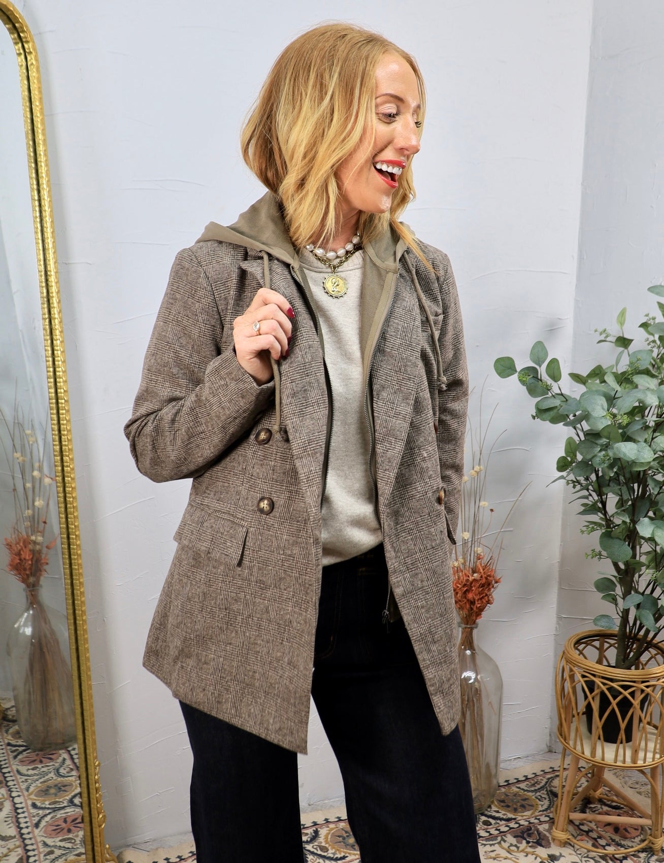 Woman wearing a brown plaid double-breasted blazer with removable hoodie layer over dark jeans