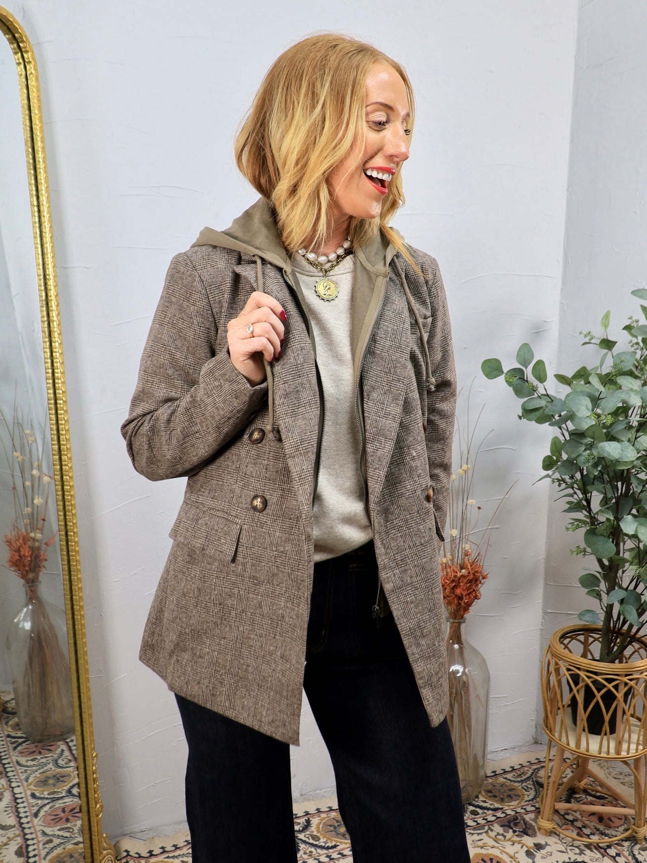 Woman wearing a brown plaid double-breasted blazer with removable hoodie layer over dark jeans