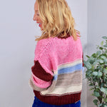 Chunky knit crewneck sweater in pink, burgundy, blue, and cream colorblock stripes, styled with blue jeans.