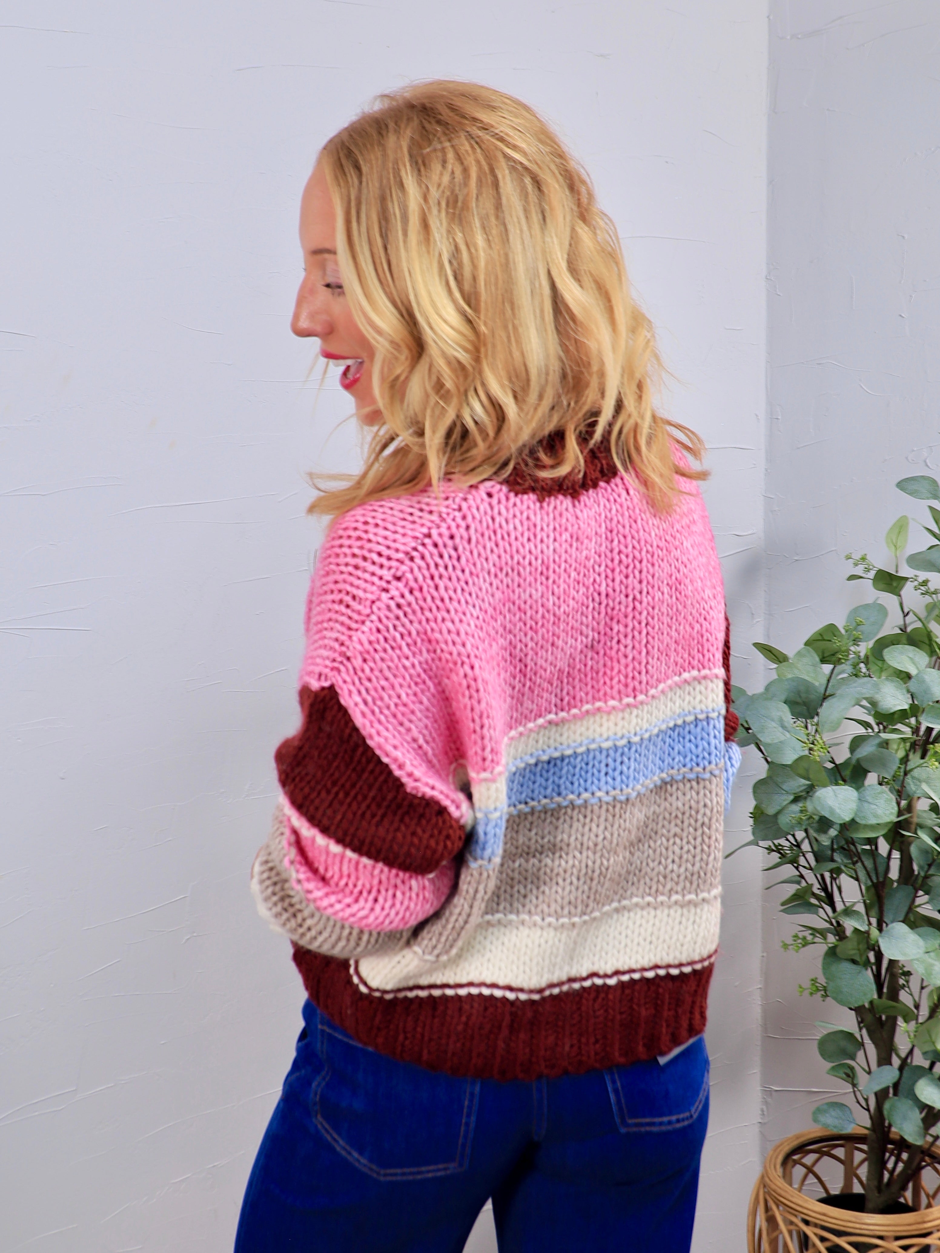 Chunky knit crewneck sweater in pink, burgundy, blue, and cream colorblock stripes, styled with blue jeans.