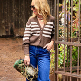 Woman wearing brown and cream striped button-front cardigan with wide-leg blue jeans and camo bag