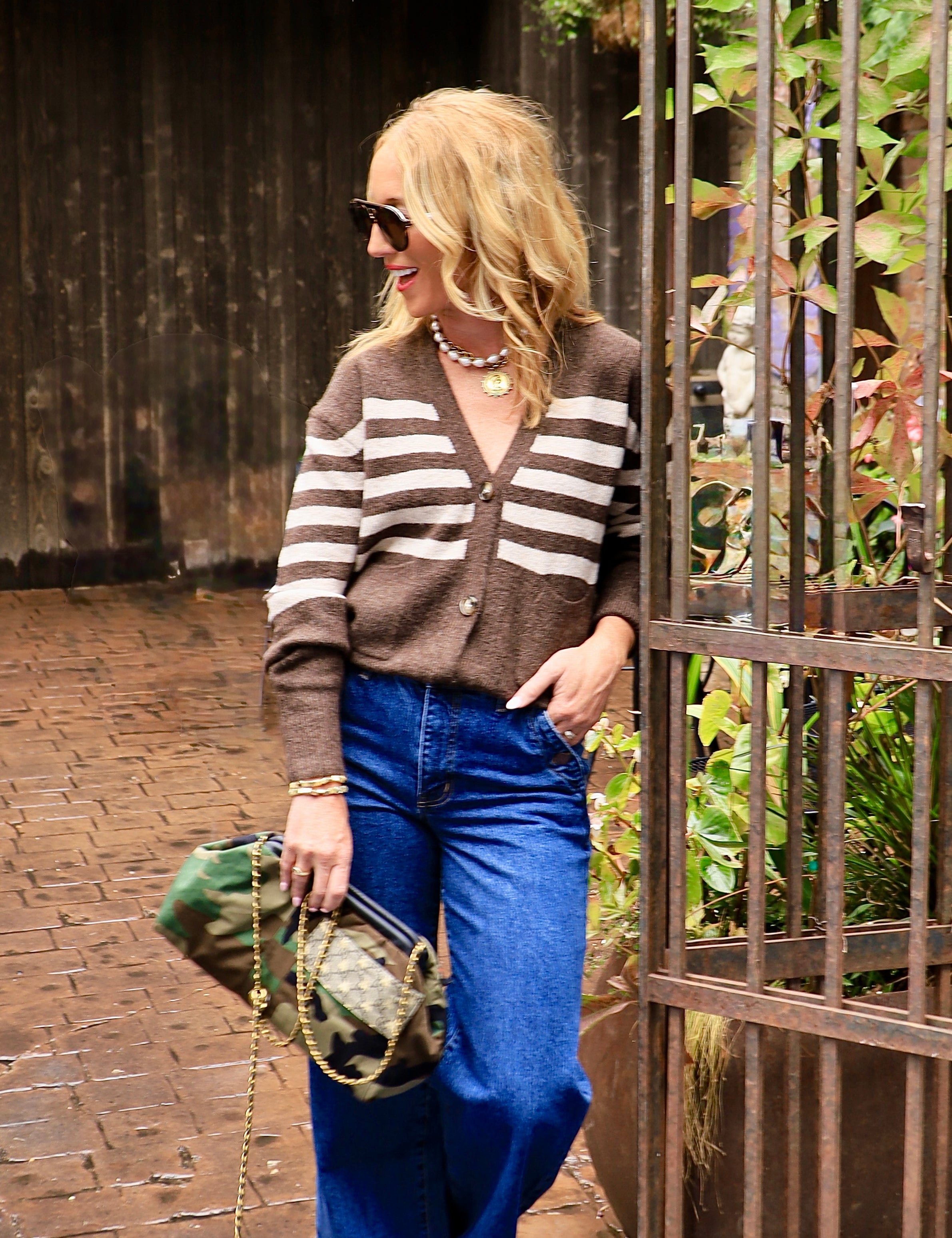 Woman wearing brown and cream striped button-front cardigan with wide-leg blue jeans and camo bag