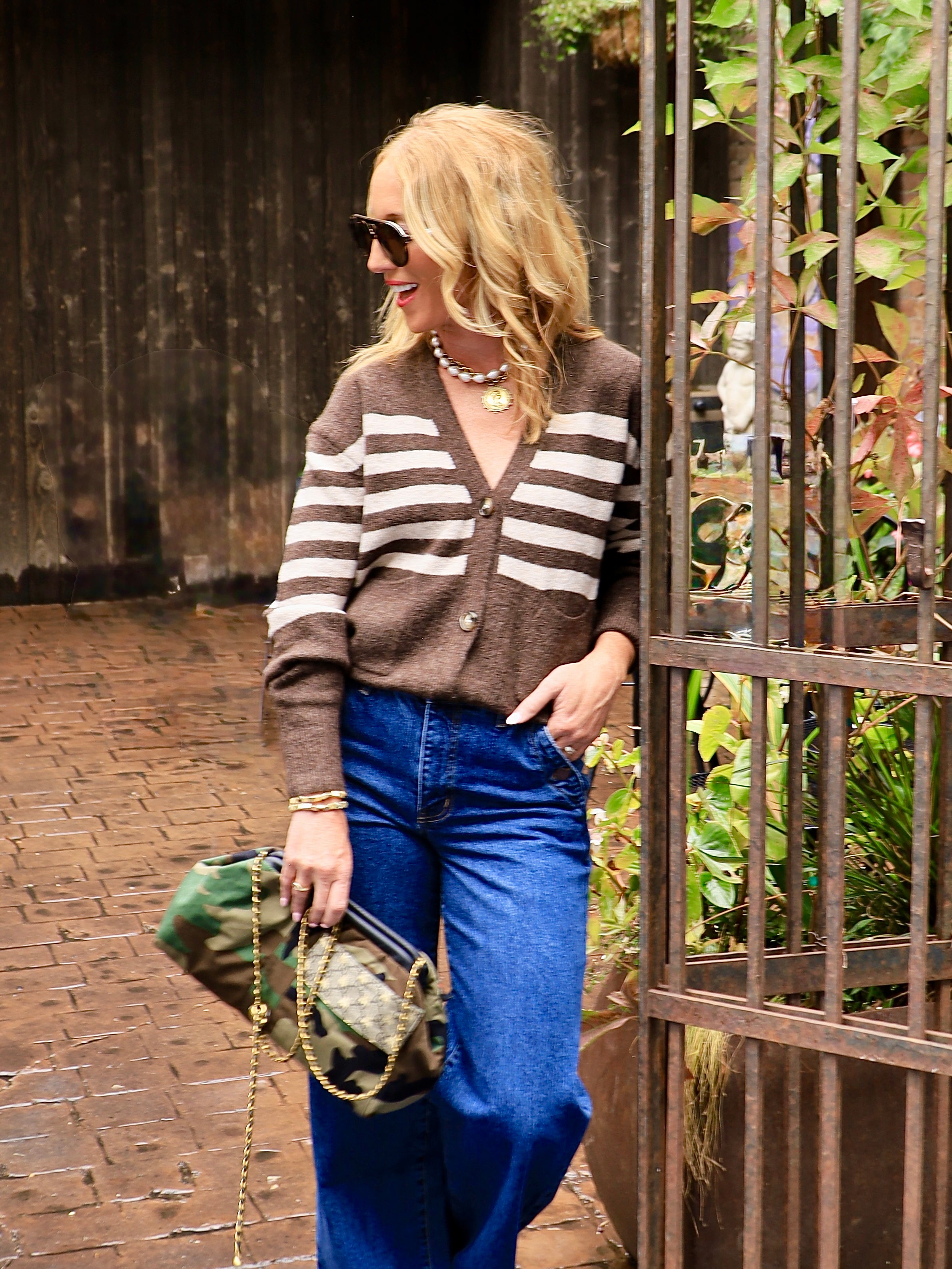 Woman wearing brown and cream striped button-front cardigan with wide-leg blue jeans and camo bag