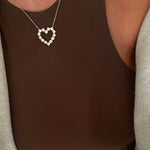 Gold chain necklace with open heart pendant set with round diamond stones, worn over brown top.