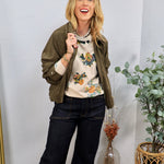 Olive green suede zip-up jacket with ruched sleeves, styled over a floral sweater and dark wide-leg jeans.